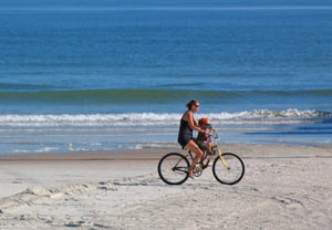 Mom and kid riding a bicycle together on the beach in New Smyrna Beach, FL. on the Foreclosures and Short Sale page of the Team Lentine website.